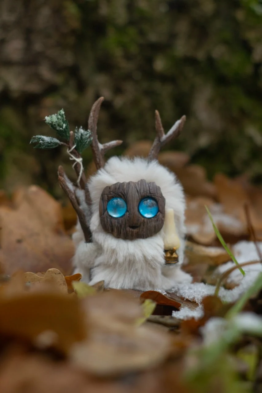 First Snow — handmade white wool Fluffy creature with brown antlers and blue glowing eyes, holding a snow-dusted fir sprig | Gnomenlands