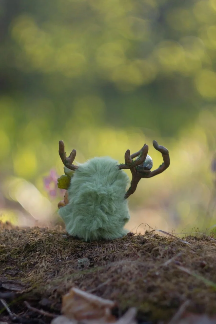 Greenhouse Keeper fluffy — back view among mossy stones and spring greenery