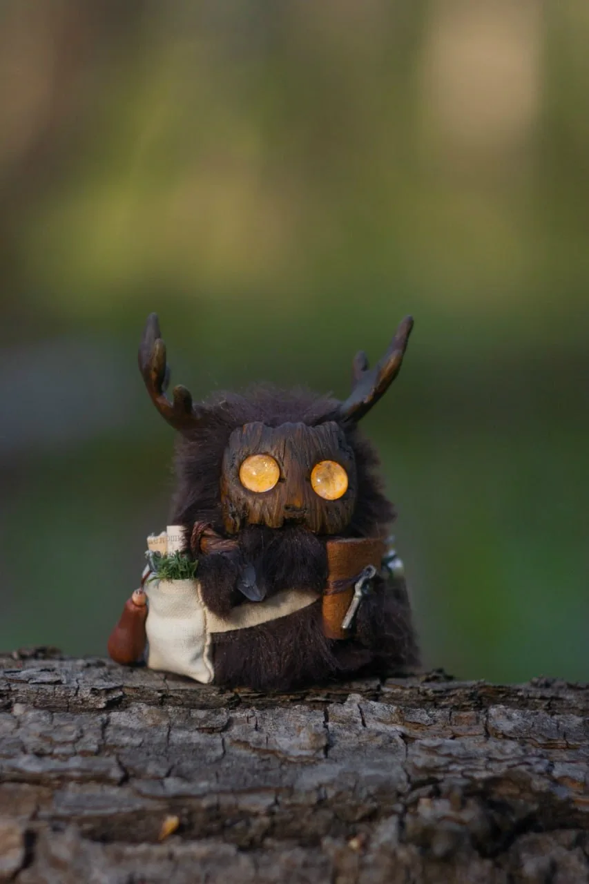The Healer — handmade dark brown wool Fluffy with glowing amber eyes, herbal satchel and notebook, sitting on forest bark | Gnomenlands Wild Garden collection
