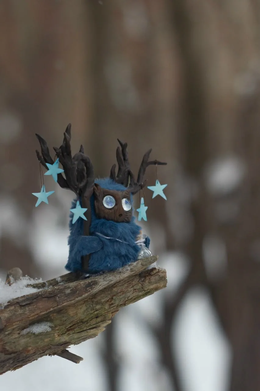 Polaris fluffy — side view sitting on a branch, stars dangling from antlers