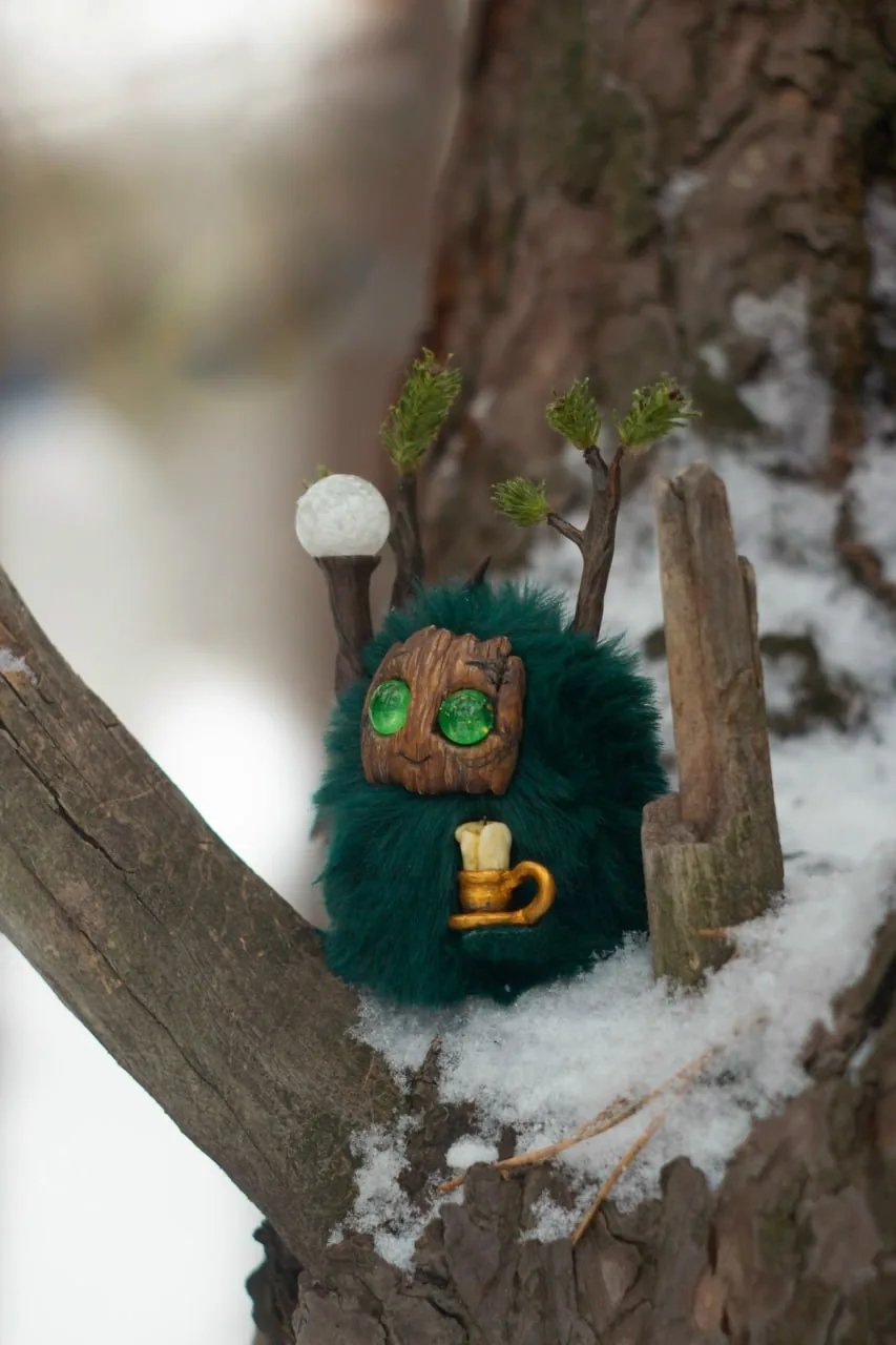 Snowy Forest — handmade dark-green wool Fluffy creature with fir-tipped antlers and a staff topped with a glowing snowglobe ball, holding a tiny mug while sitting in snowy pine branches | Gnomenlands
