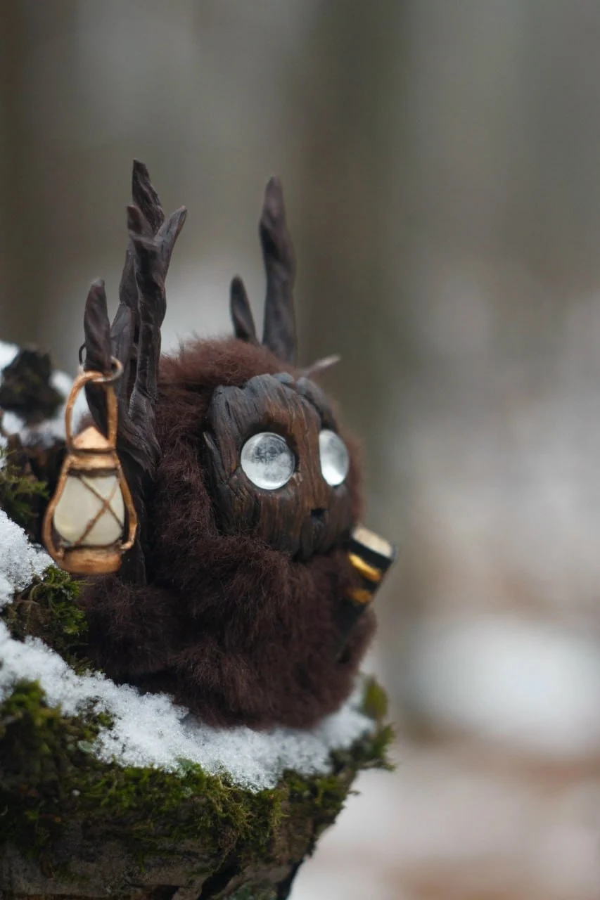 Storyteller — handmade dark-brown wool Fluffy creature with branching antlers, lantern and golden book on a snowy mossy stump | Gnomenlands