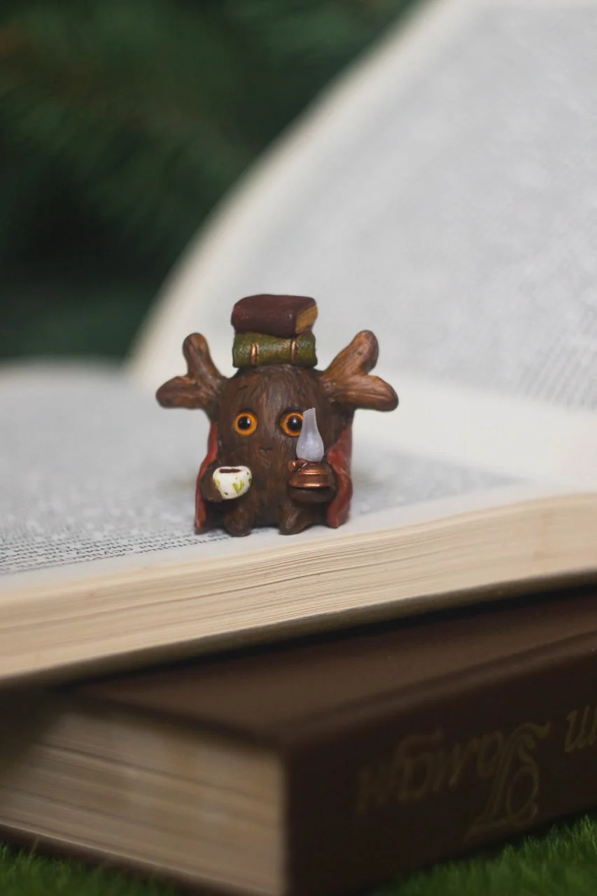 Forest Sprite Bookworm resting on open book pages — tiny handmade polymer clay miniature
