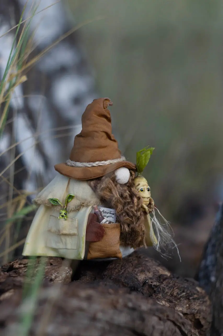 Handmade gnome in beige cloak with plants in forest