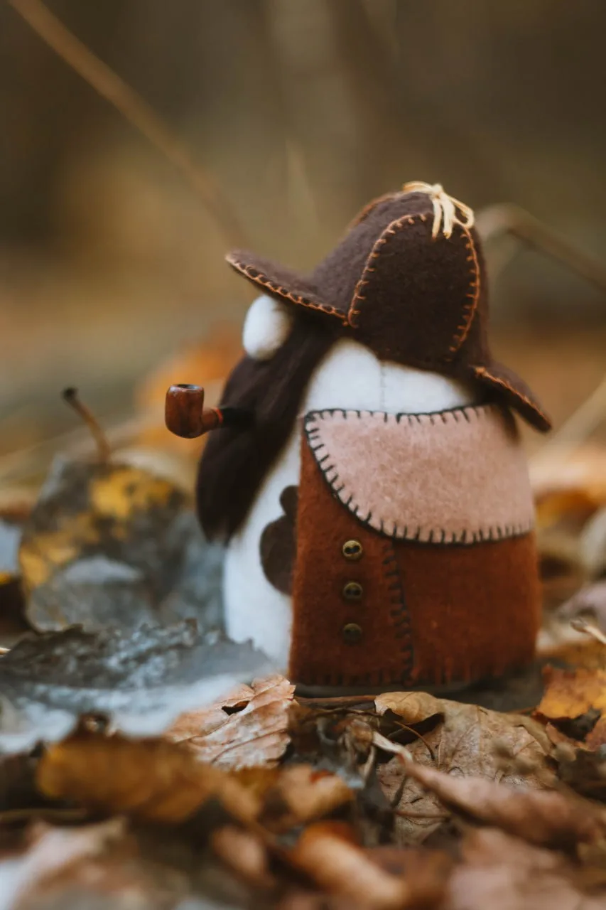 Collectible Gnome Sherlock Holmes with magnifier and pipe in autumn forest