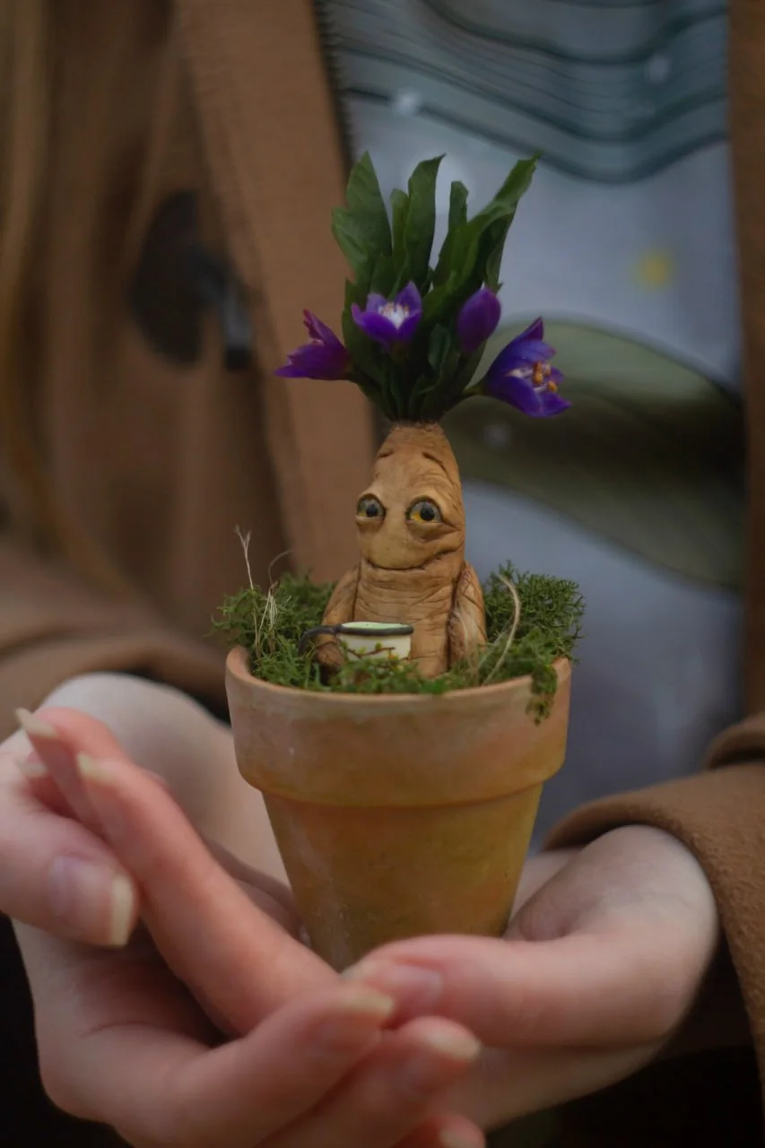 Mandrake in terracotta pot with purple flowers held in hands — polymer clay magical figurine