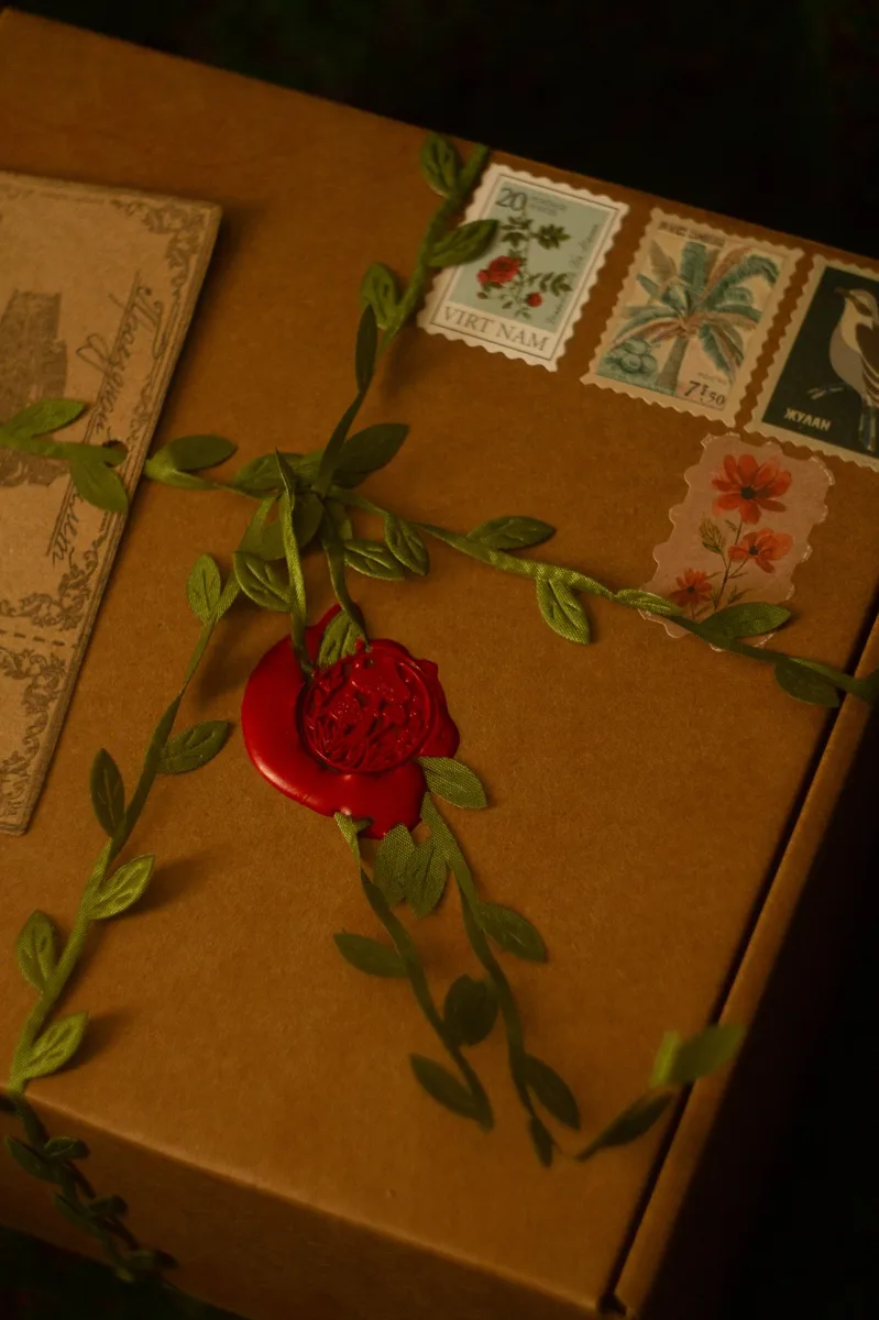 Gnomenlands packaging detail — close-up of red wax rose seal and vintage botanical postage stamps on kraft box
