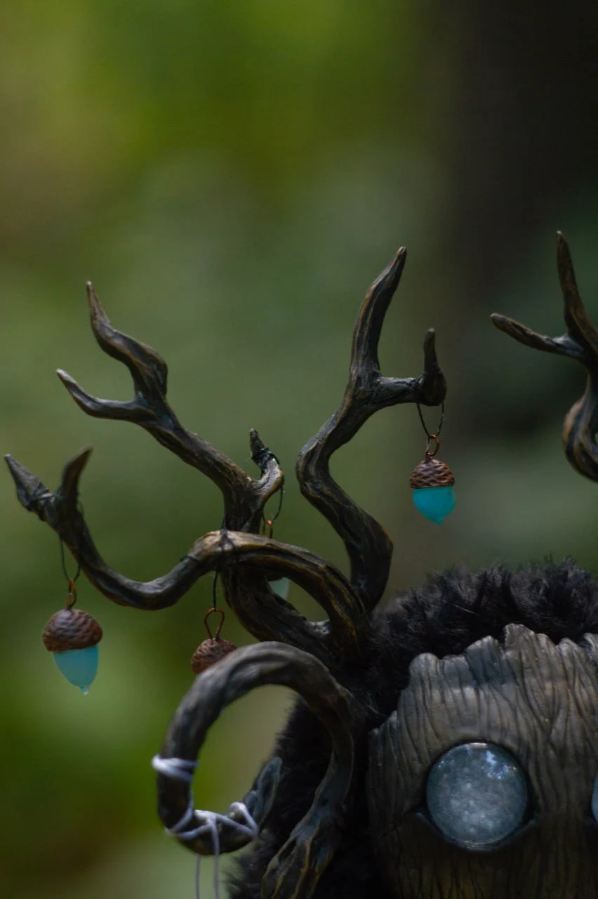 Close-up of glowing teal clay acorn lanterns and crescent moon pendant on Wood Spirit antlers