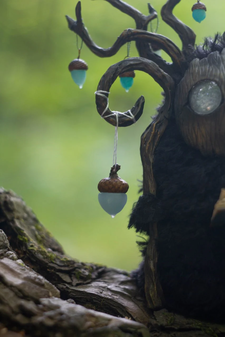 Wood Spirit Midnight Light — back view, dark plush fur body with large branching antlers and hanging glowing acorns against forest background