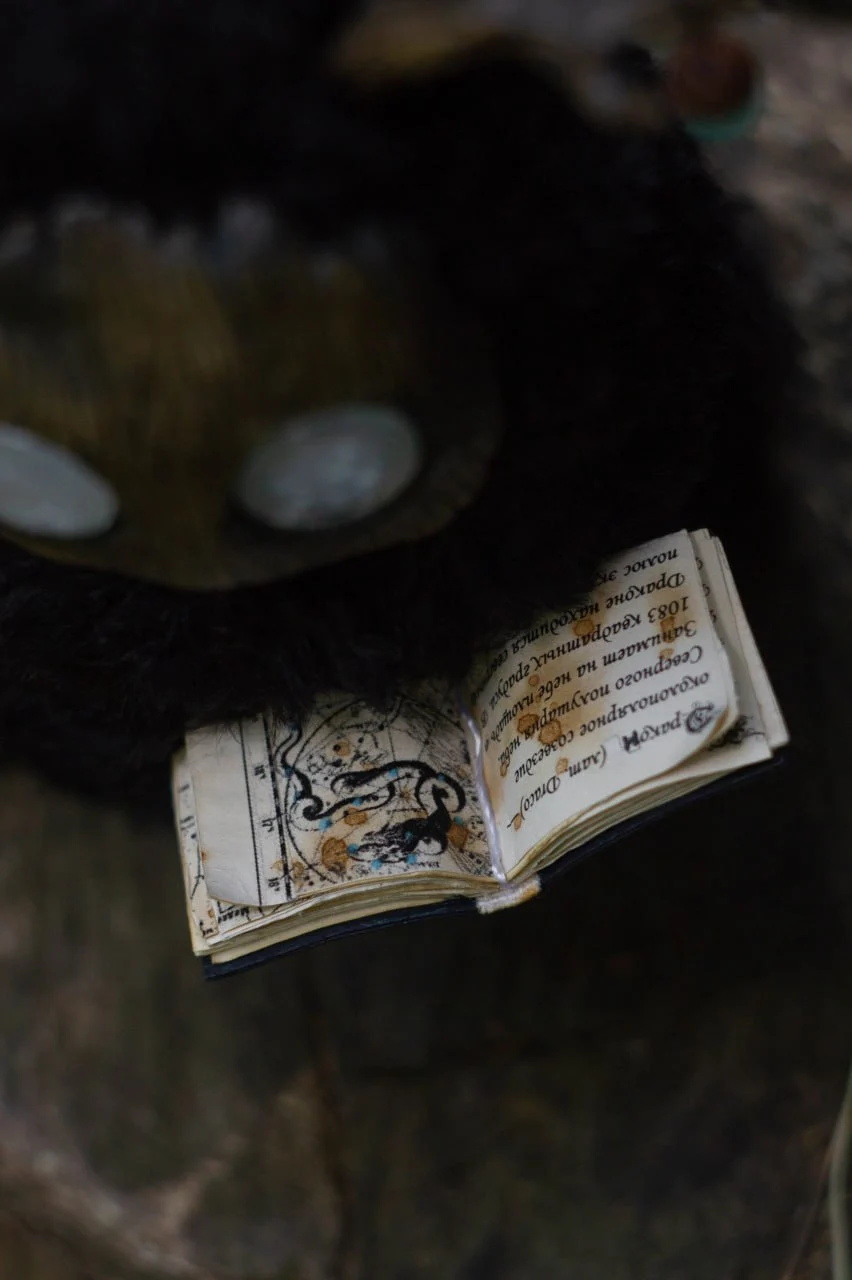Wood Spirit Midnight Light holding an open ancient star atlas — miniature handmade book with constellation illustrations
