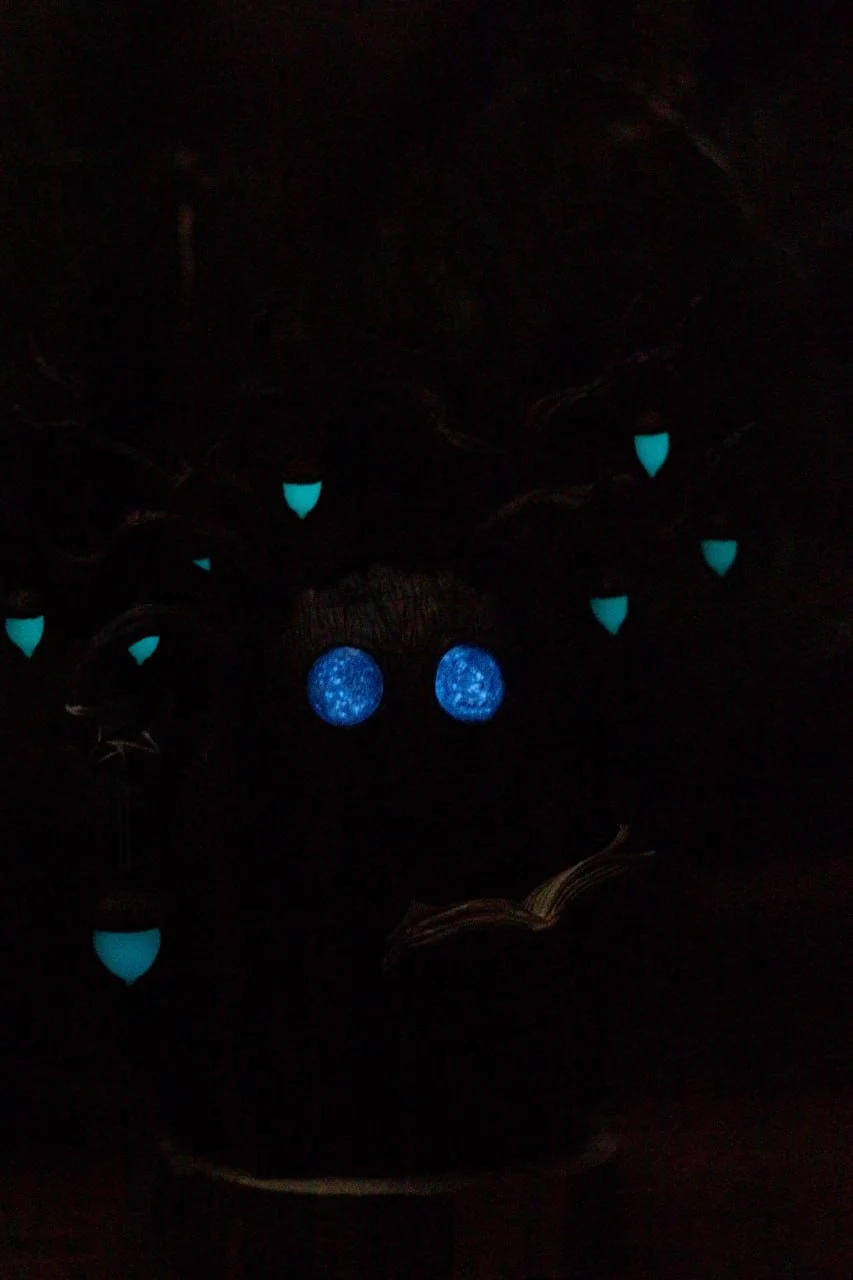 Wood Spirit Midnight Light in the dark — glowing blue eyes and teal acorn lanterns visible in complete darkness, magical glow effect