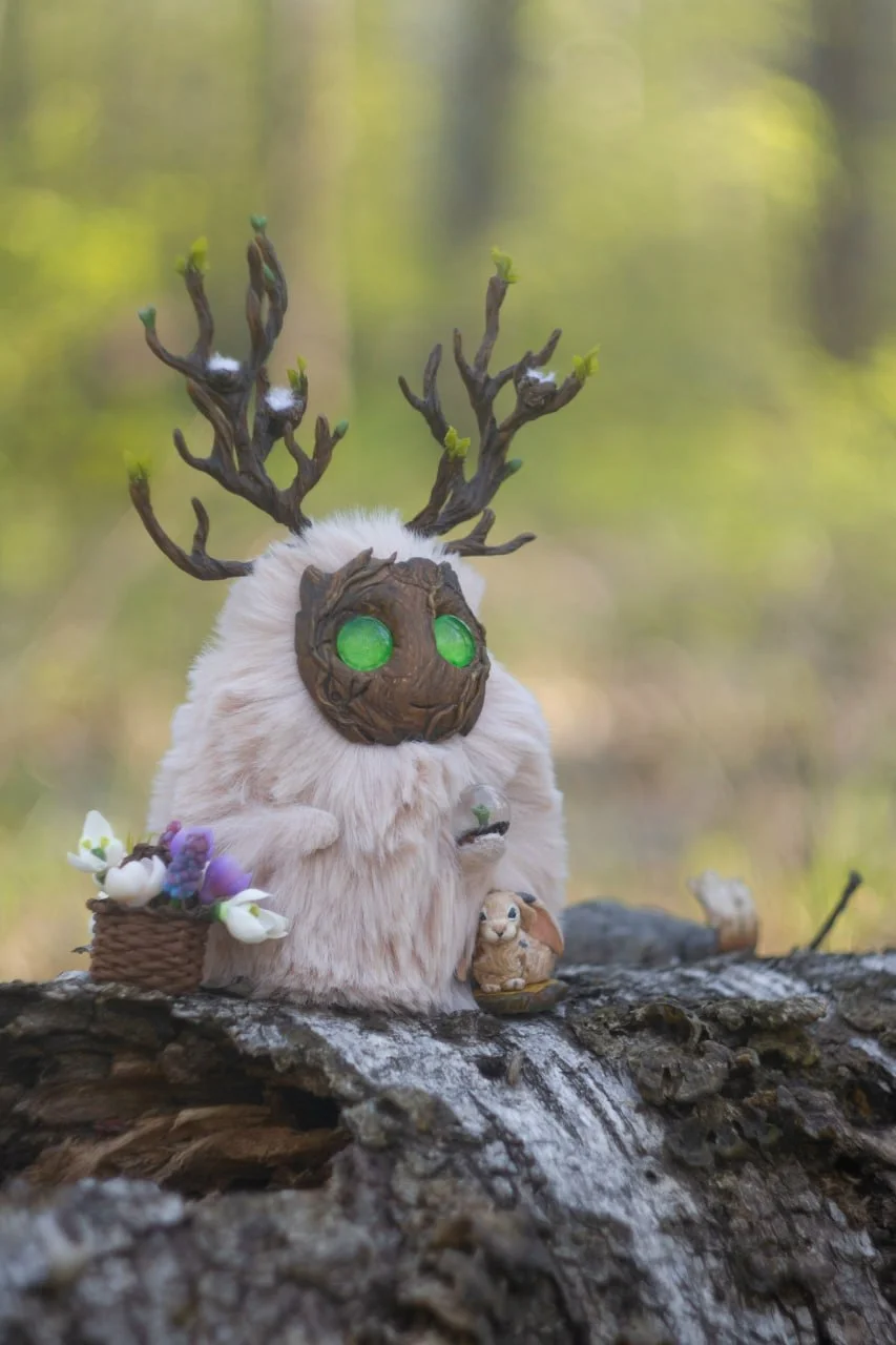 Wood Spirit Ostara's Breath — full front view, pale fur body, budding antlers, basket of snowdrops, glass orb with green sprout, hare at base on birch log